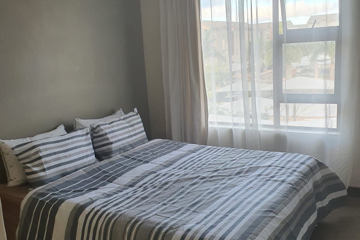 A functional bedroom featuring neutral wall tones, carpeted flooring, and a large window allowing natural light.