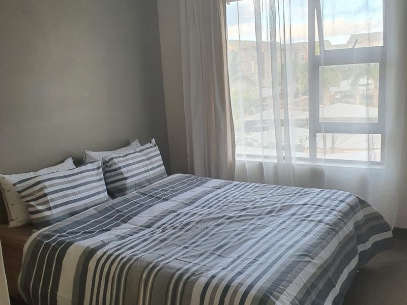 A functional bedroom featuring neutral wall tones, carpeted flooring, and a large window allowing natural light.