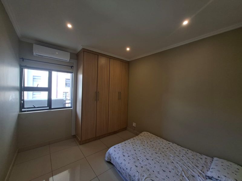 A bedroom featuring tiled flooring, built-in wooden cupboards, and an integrated air conditioning unit.