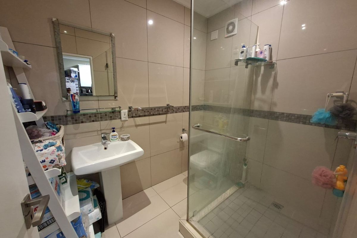 A modern bathroom featuring a pedestal basin, a glass-enclosed shower, and neutral floor-to-ceiling wall tiles.