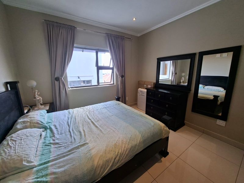 A bedroom featuring tiled flooring, recessed downlighting, and an aluminium-framed window with neutral wall finishes.