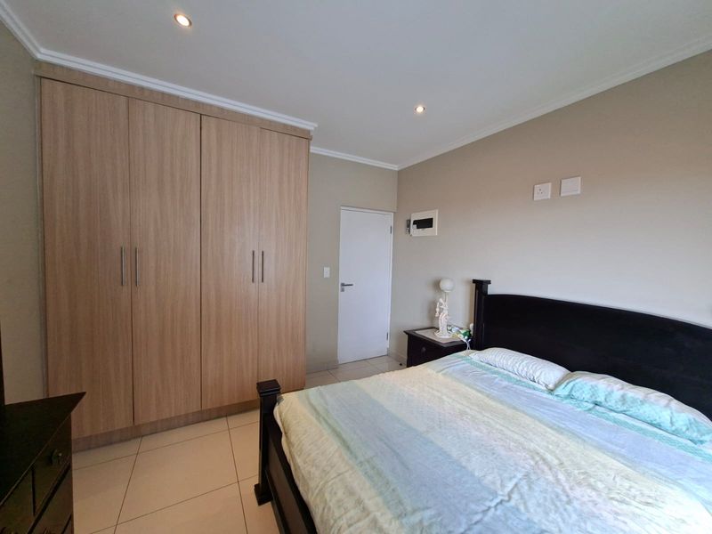A well-maintained bedroom featuring light wood-finish built-in cupboards, neutral wall tones, tiled flooring, and recessed ceiling lighting.