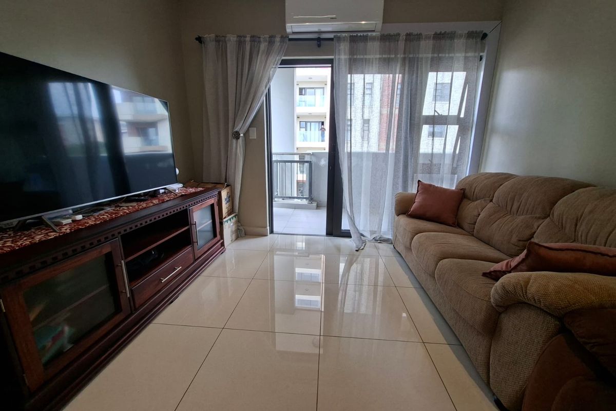 A well-maintained living room featuring polished tile flooring, a wall-mounted air conditioning unit, and direct access to a private balcony through sliding glass doors.