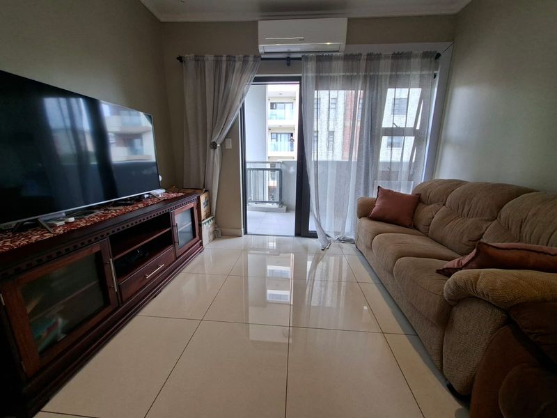 A well-maintained living room featuring polished tile flooring, a wall-mounted air conditioning unit, and direct access to a private balcony through sliding glass doors.