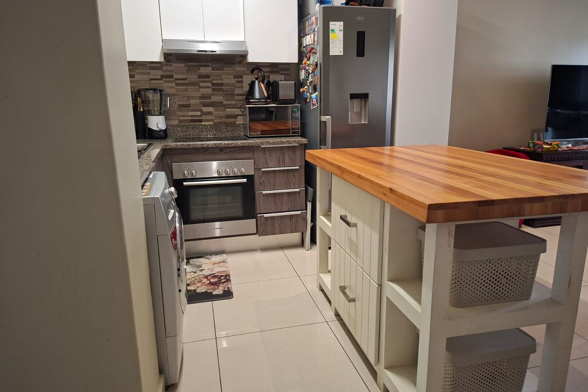 Compact kitchen featuring built-in oven, extractor fan, granite countertops, tiled backsplash, and modern cabinetry with a central wooden-topped island unit.