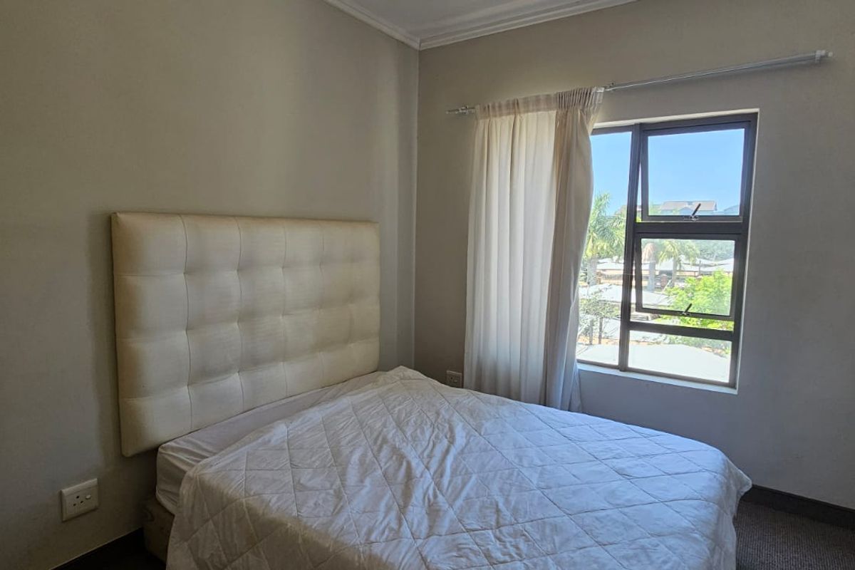 A functional bedroom featuring neutral wall tones, a large window with natural light, and a built-in curtain rail.