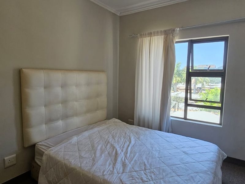 A functional bedroom featuring neutral wall tones, a large window with natural light, and a built-in curtain rail.