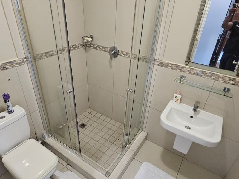A clean and functional bathroom featuring a glass shower enclosure, pedestal basin, and toilet with neutral wall and floor tiling.