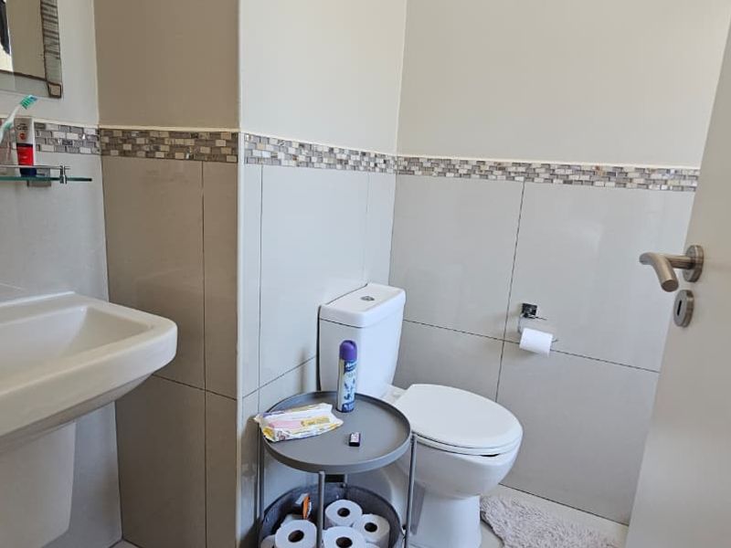 A functional bathroom featuring a pedestal washbasin, chrome mixer tap, ceramic toilet, and decorative mosaic tile accents on the walls.