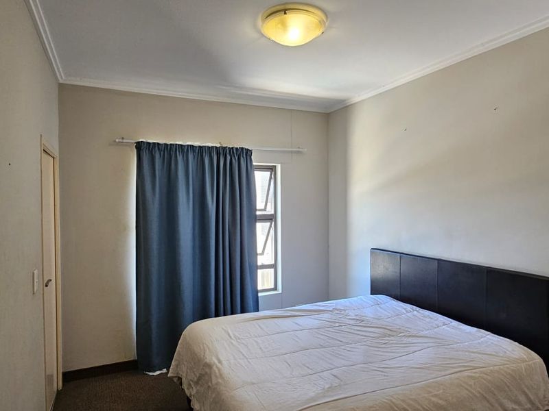 A standard bedroom featuring carpeted flooring, a central ceiling light, and a window with curtain track, presenting a neutral canvas for potential updates.