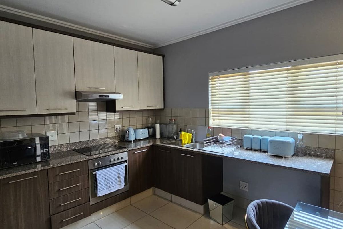 A functional kitchen featuring two-tone cabinetry, granite countertops, a built-in oven with hob, extractor fan, and a tiled backsplash with natural light.