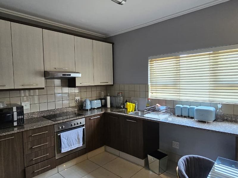 A functional kitchen featuring two-tone cabinetry, granite countertops, a built-in oven with hob, extractor fan, and a tiled backsplash with natural light.