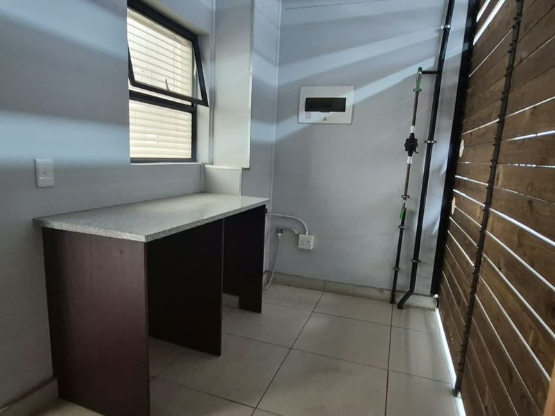 A functional laundry area featuring tiled flooring, a built-in counter, and dedicated plumbing and electrical connections for appliances.