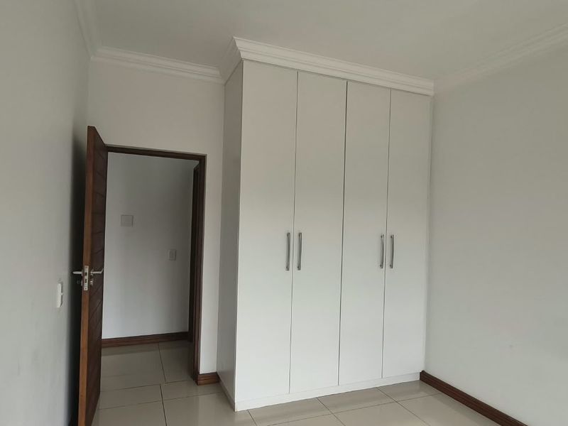 A clean, empty bedroom featuring neutral tiled flooring, white walls, and a modern built-in wardrobe with sleek handles.