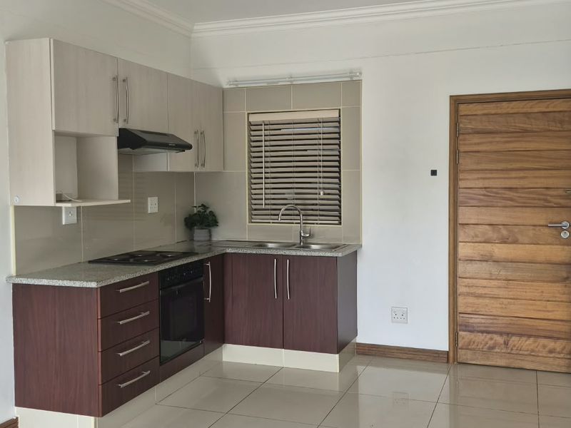A clean, functional kitchen featuring two-tone cabinetry, granite countertops, built-in oven and hob, and tiled flooring, presenting a well-maintained and practical cooking space.