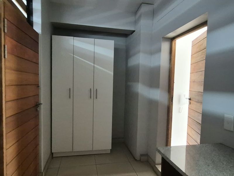 A clean, modern hallway featuring tiled flooring, a built-in white wardrobe, and wooden doors leading to adjacent rooms.