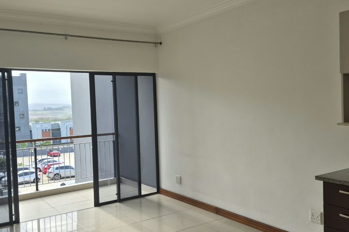 An open-plan living area featuring tiled floors, modern kitchen cabinetry with granite countertops, and sliding doors leading to a private balcony.