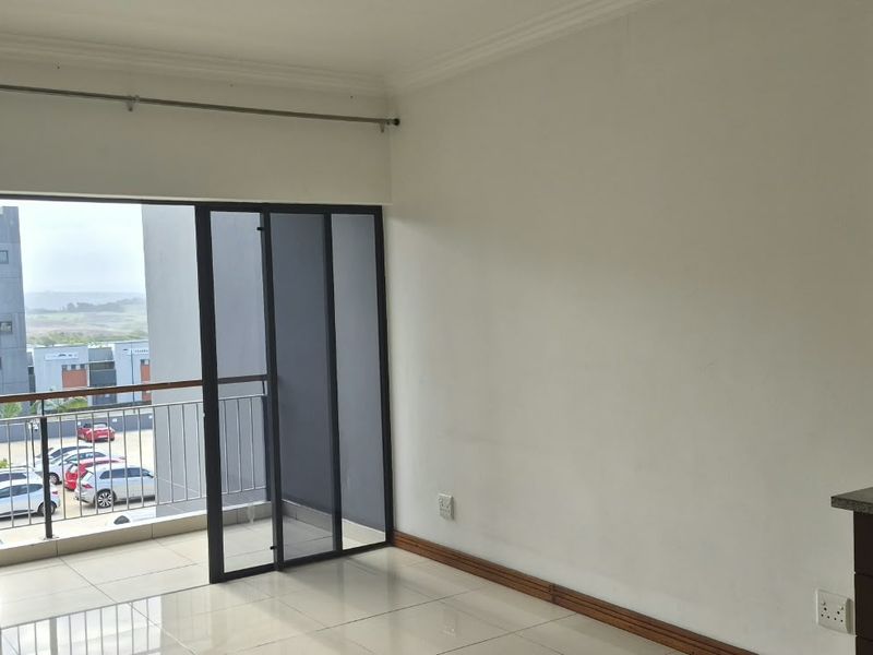 An open-plan living area featuring tiled floors, modern kitchen cabinetry with granite countertops, and sliding doors leading to a private balcony.