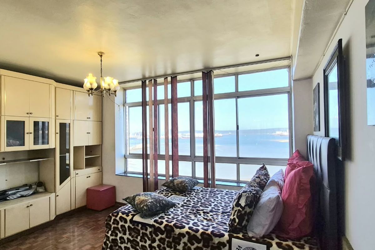 Bedroom featuring extensive built-in cabinetry, parquet flooring, and large windows offering natural light and coastal views.
