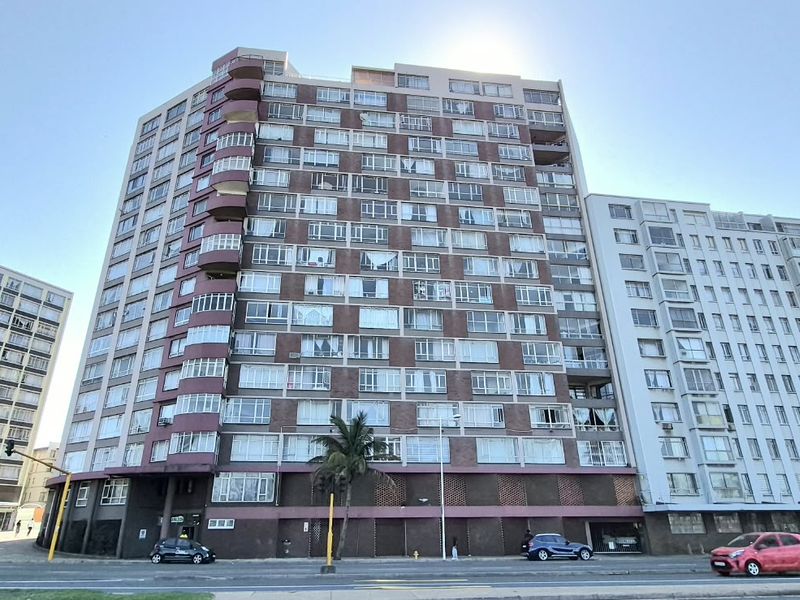 A multi-story apartment building featuring a brick facade, numerous balconies, and large windows, situated along a street front.
