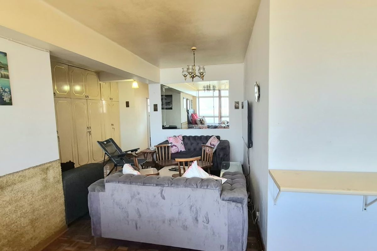 A living room area featuring built-in storage cupboards, a wall-mounted mirror, and a wall-mounted shelf, showing signs of wear on the ceiling and walls.