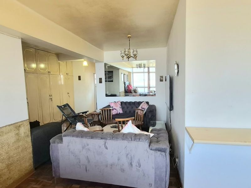 A living room area featuring built-in storage cupboards, a wall-mounted mirror, and a wall-mounted shelf, showing signs of wear on the ceiling and walls.