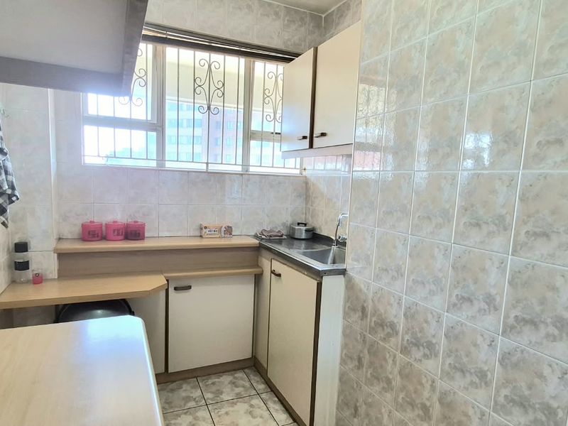 A compact, functional kitchen featuring built-in cabinetry, a stainless steel sink, and tiled wall finishes, offering potential for a modern renovation.