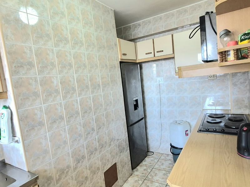 A functional kitchen featuring built-in cabinetry, a stainless steel sink, tiled backsplash, and an electric hob, offering a practical layout for daily use.