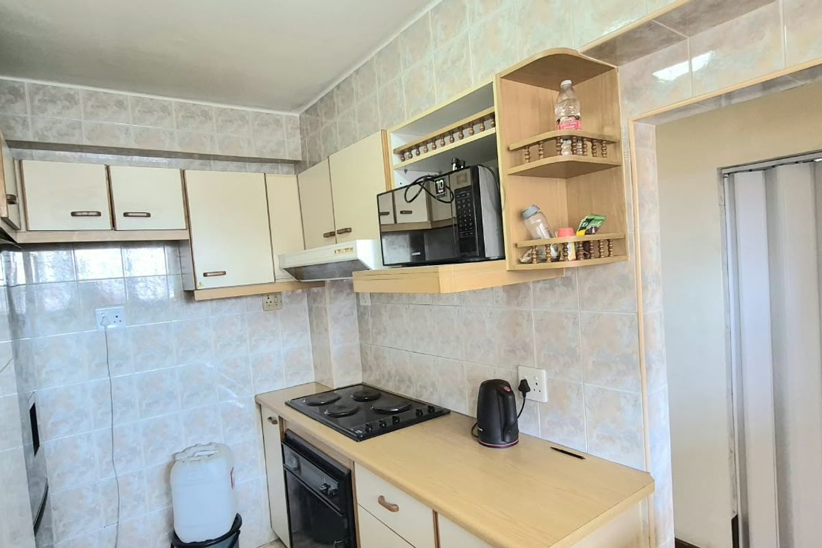 A compact kitchen featuring tiled walls, built-in cabinetry, and integrated cooking appliances, offering a functional layout with potential for modern updates.