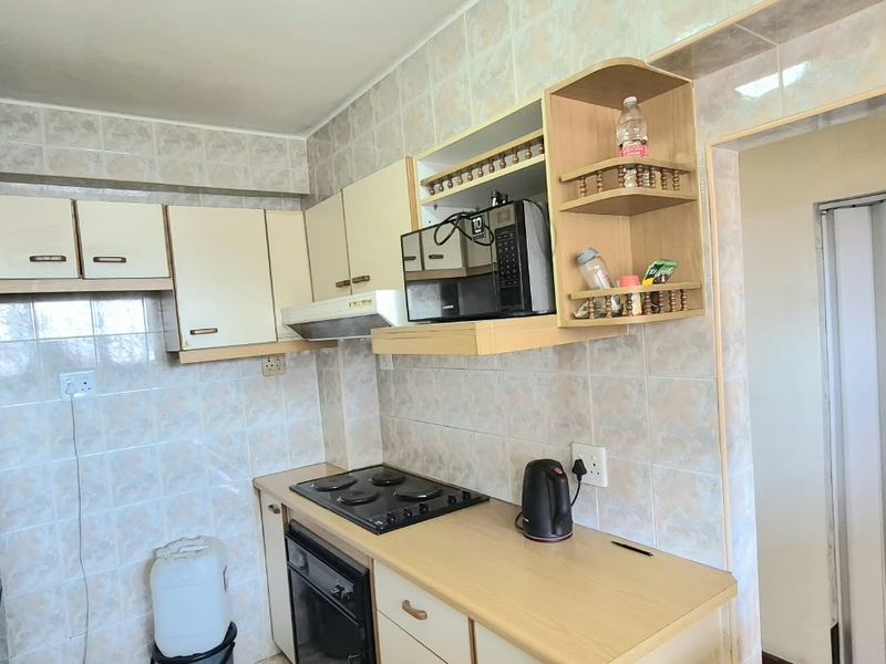 A compact kitchen featuring tiled walls, built-in cabinetry, and integrated cooking appliances, offering a functional layout with potential for modern updates.
