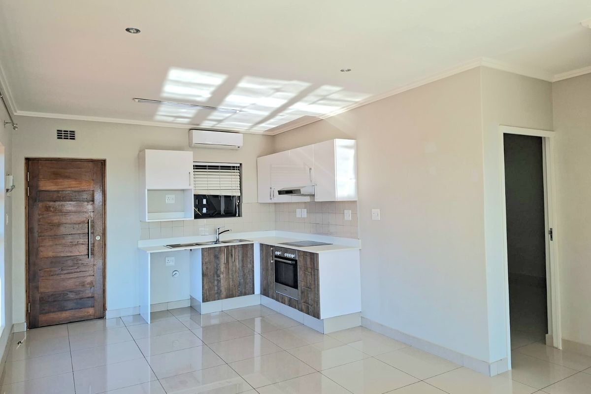 Modern open-plan kitchen featuring built-in cabinetry, integrated oven and hob, tiled flooring, and a split-system air conditioner in a bright, neutral space.