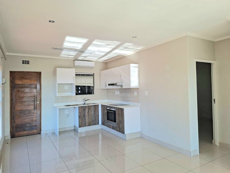 Modern open-plan kitchen featuring built-in cabinetry, integrated oven and hob, tiled flooring, and a split-system air conditioner in a bright, neutral space.