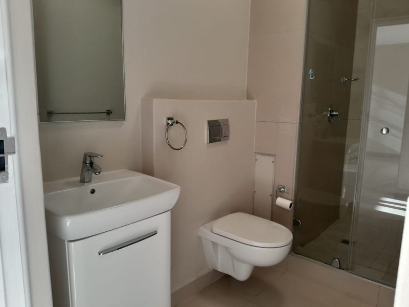 Modern bathroom featuring a wall-mounted toilet, vanity basin with mixer tap, and a glass-enclosed shower with neutral tiling.