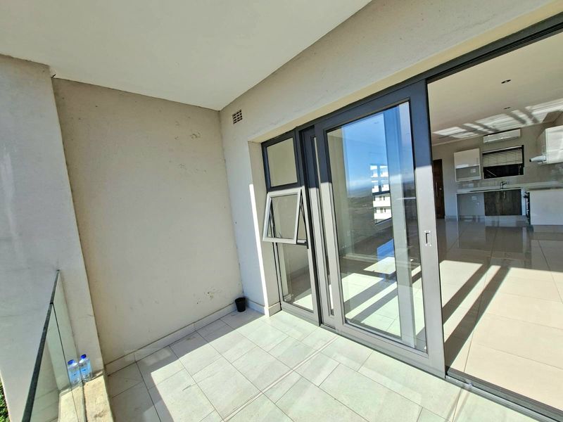A clean, tiled balcony featuring a modern glass balustrade and large sliding doors providing seamless access to the interior living space.