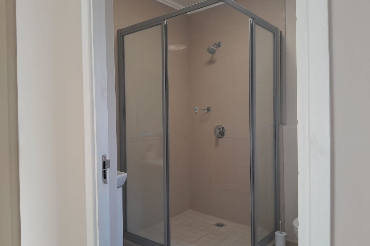 A functional bathroom featuring a corner shower enclosure with tiled walls and flooring, presenting a clean and neutral space.