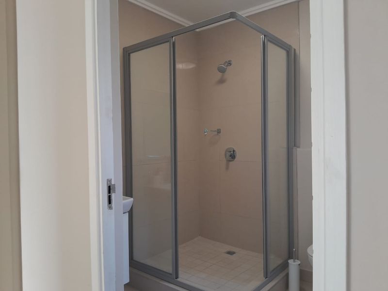 A functional bathroom featuring a corner shower enclosure with tiled walls and flooring, presenting a clean and neutral space.