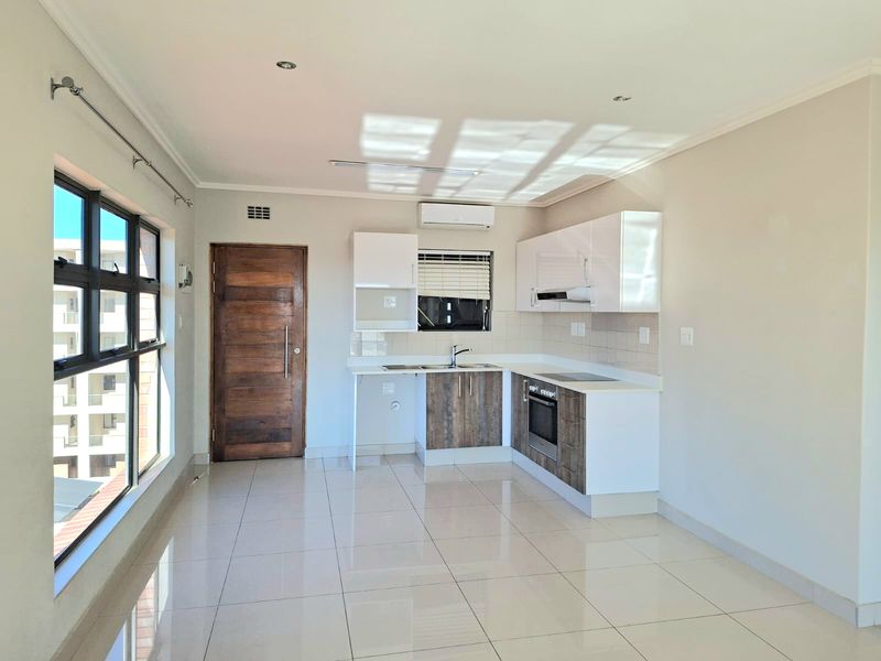 Modern open-plan kitchen featuring sleek cabinetry, built-in oven and hob, tiled flooring, and an integrated air conditioning unit in a bright, neutral space.