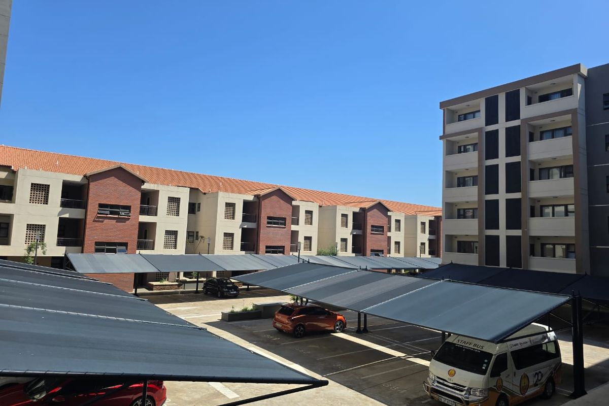 View of the apartment complex exterior featuring multiple covered parking bays and multi-story residential buildings with brick and plaster finishes.