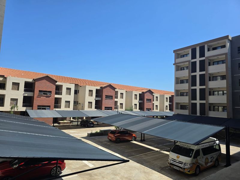 View of the apartment complex exterior featuring multiple covered parking bays and multi-story residential buildings with brick and plaster finishes.