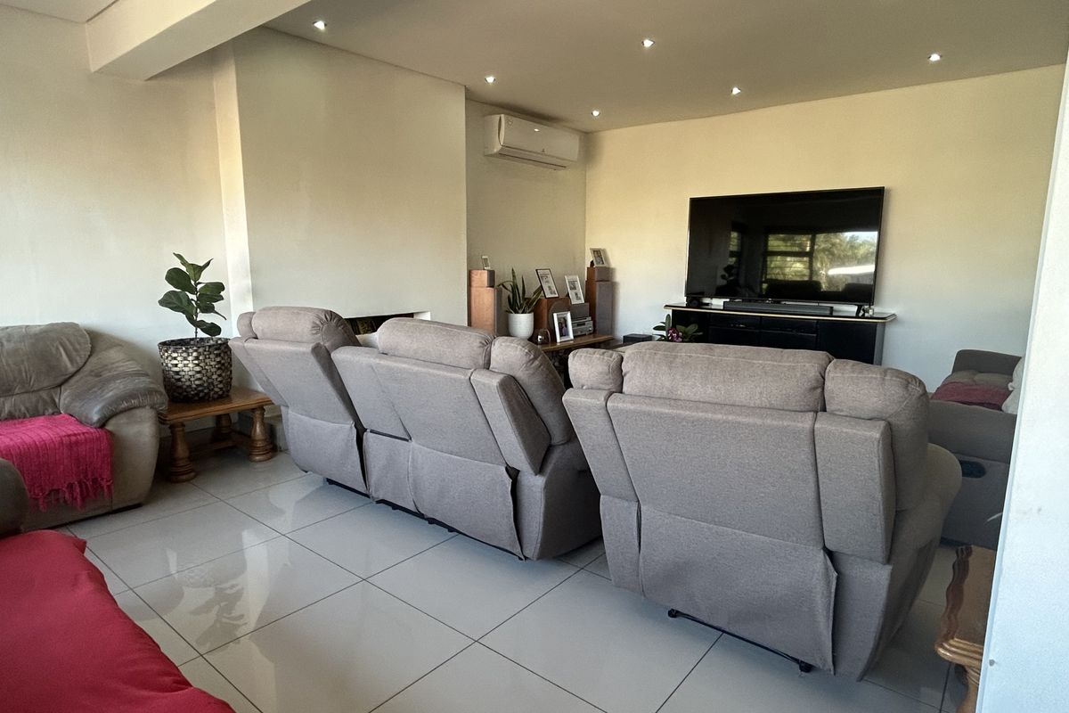 A spacious living room featuring large format floor tiles, recessed downlighting, and a wall-mounted split-system air conditioner.