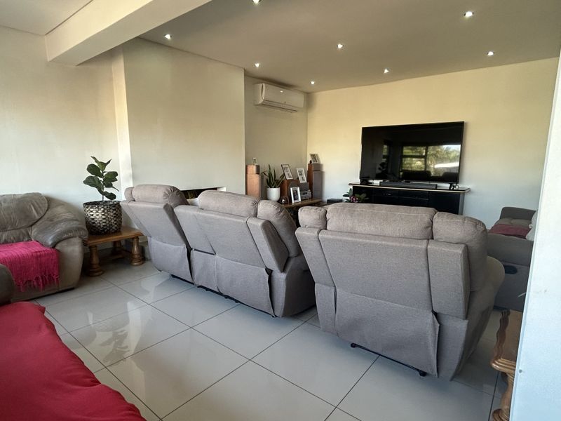 A spacious living room featuring large format floor tiles, recessed downlighting, and a wall-mounted split-system air conditioner.
