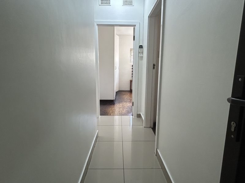 A clean, neutral hallway featuring light-colored floor tiles and access to adjacent rooms, providing a bright and functional transition space.