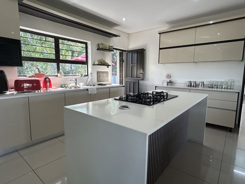 Modern kitchen featuring a central island with a gas cooktop, sleek cabinetry, tiled flooring, and ample natural light from the large window.