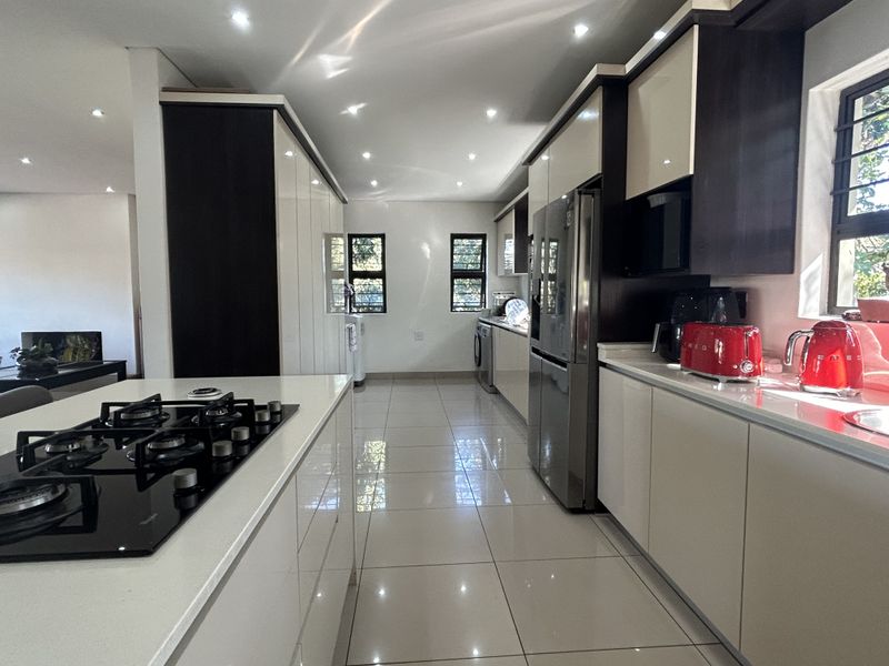 Modern kitchen featuring a central island with a gas hob, sleek high-gloss cabinetry, stone countertops, and polished tiled flooring with recessed lighting.