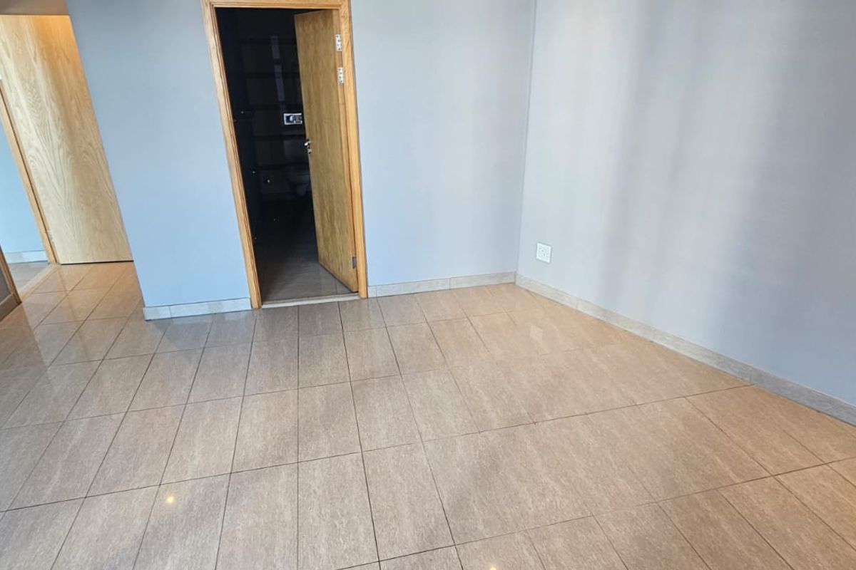 A bright, empty living area featuring neutral grey walls, modern tiled flooring, and clean wooden door frames, ready for personalization.