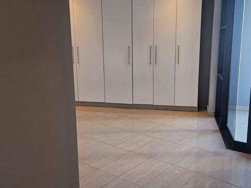 A bright, empty bedroom featuring modern built-in cupboards, tiled flooring, and direct access to a private balcony through a sliding glass door.
