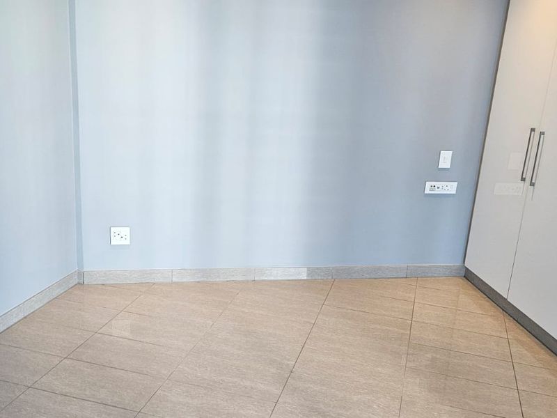 A clean, empty bedroom featuring neutral wall paint, modern tiled flooring, and ample built-in cupboard storage space.