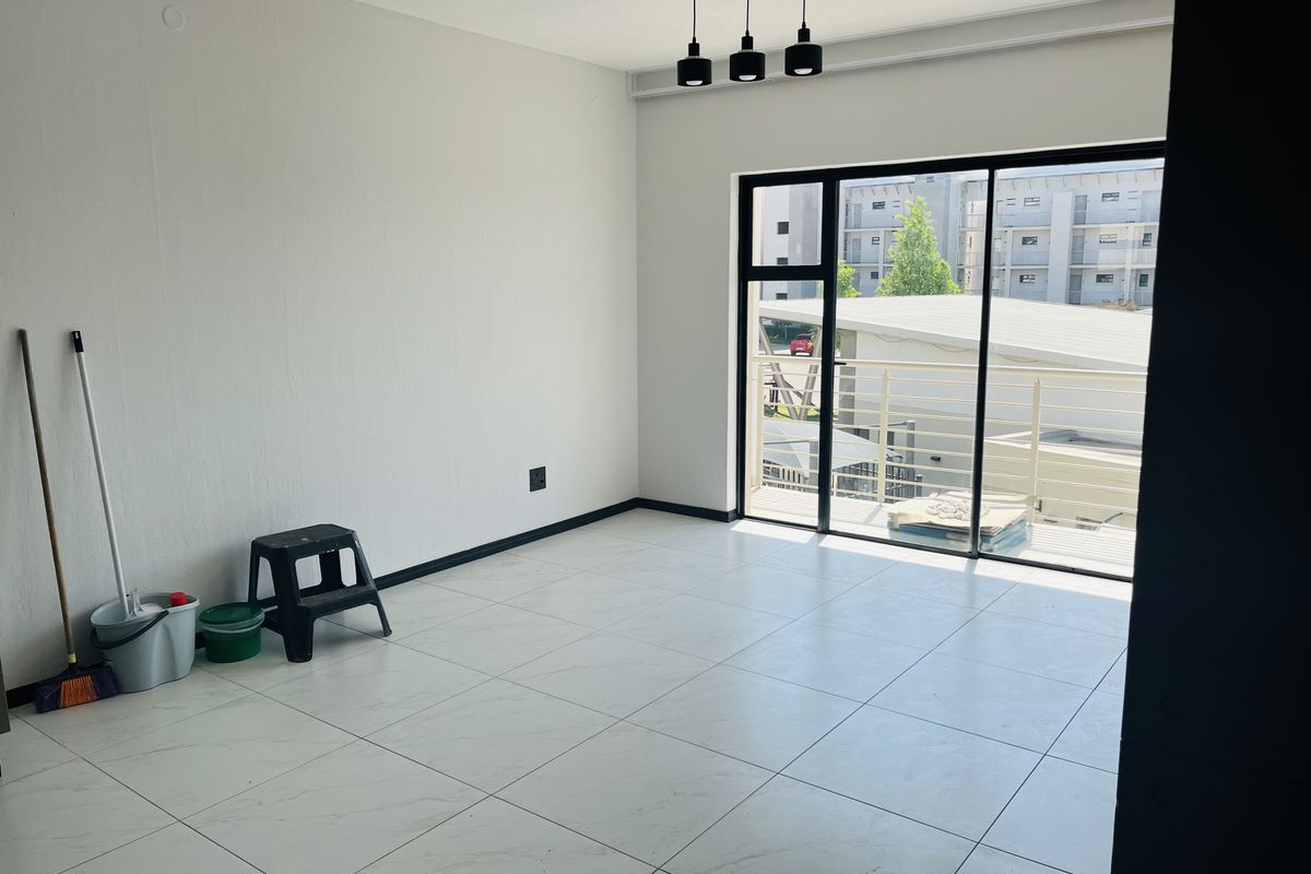 A bright, empty living area featuring modern white tiled flooring, contemporary pendant lighting, and a large sliding glass door leading to a balcony.