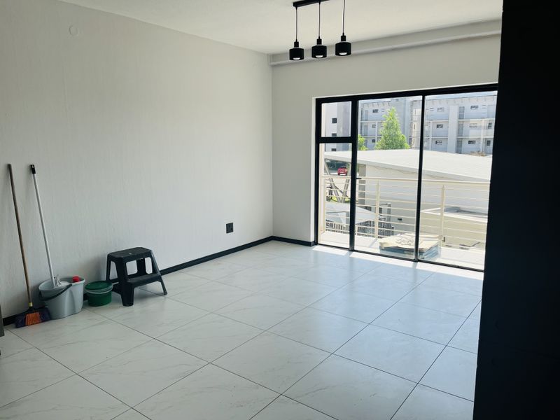 A bright, empty living area featuring modern white tiled flooring, contemporary pendant lighting, and a large sliding glass door leading to a balcony.