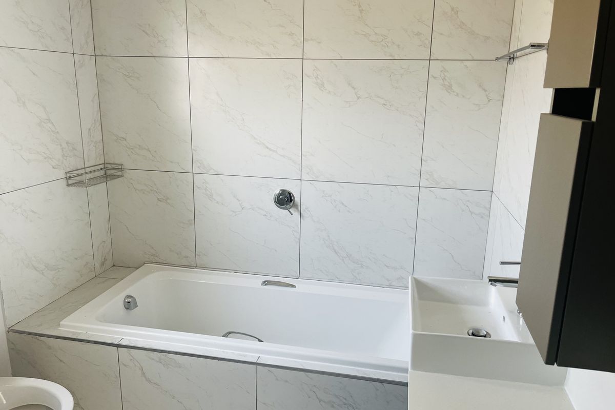 Modern bathroom featuring a built-in bathtub, wall-mounted basin, and elegant marble-look wall tiling throughout.
